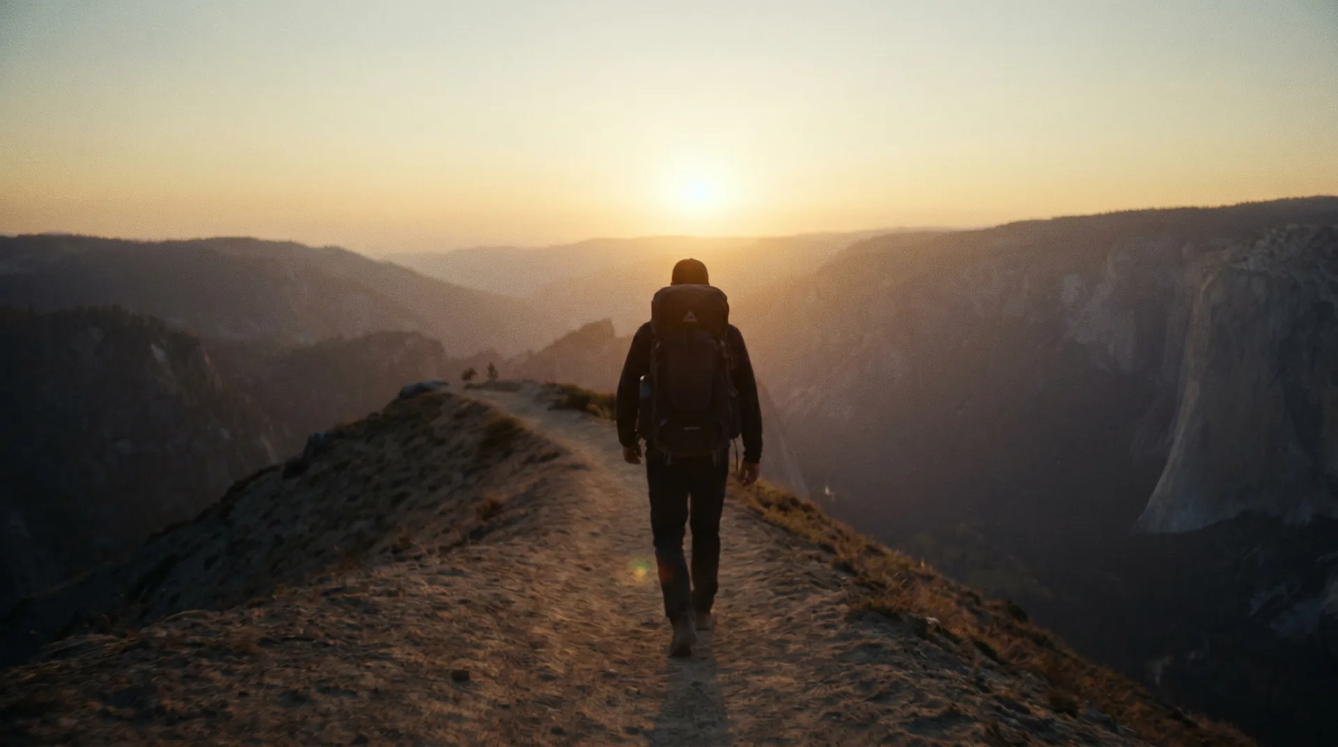 A hiker walking a high ridge trail toward a low amber sun at golden hour