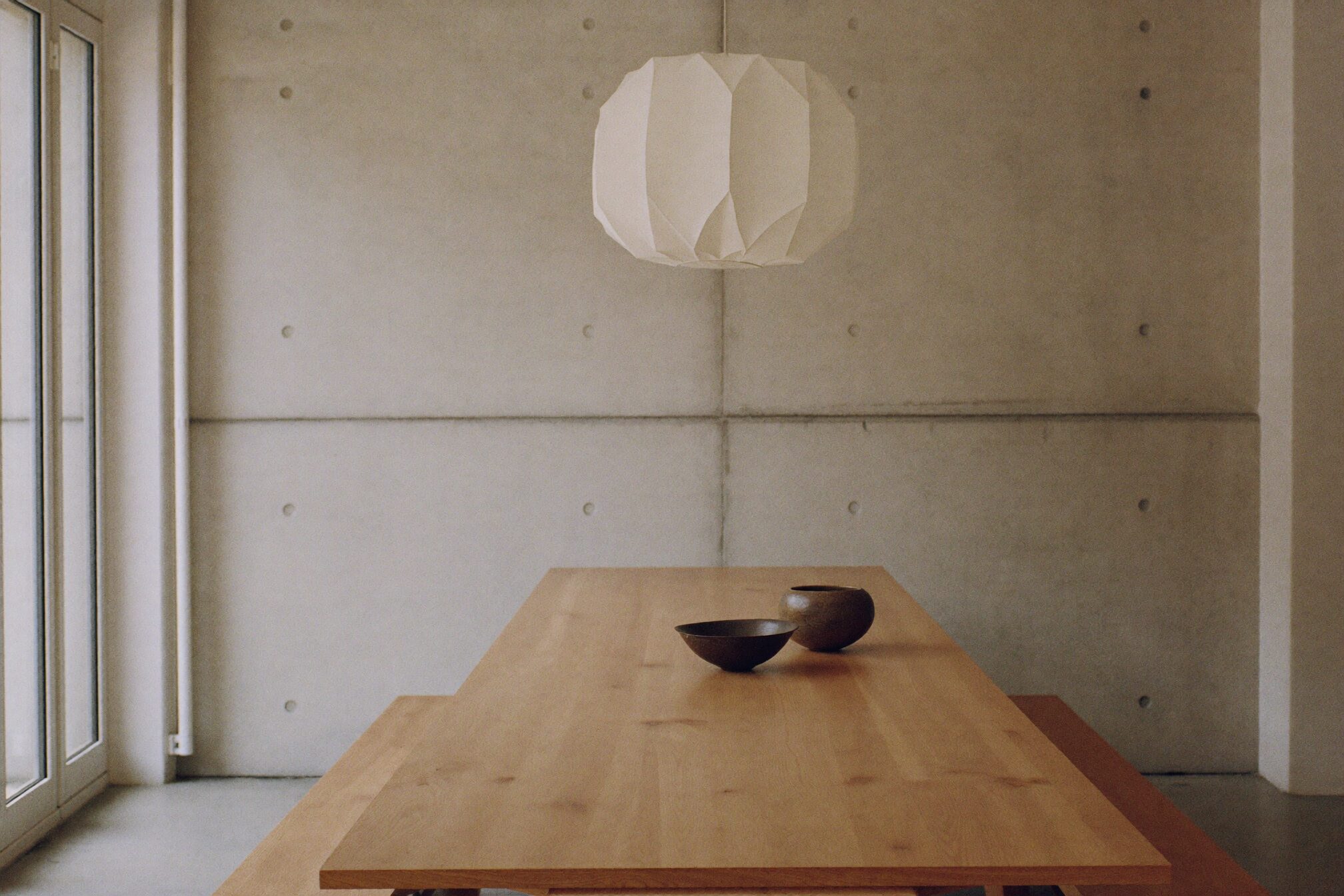 Oak dining table with paper pendant lamp against concrete